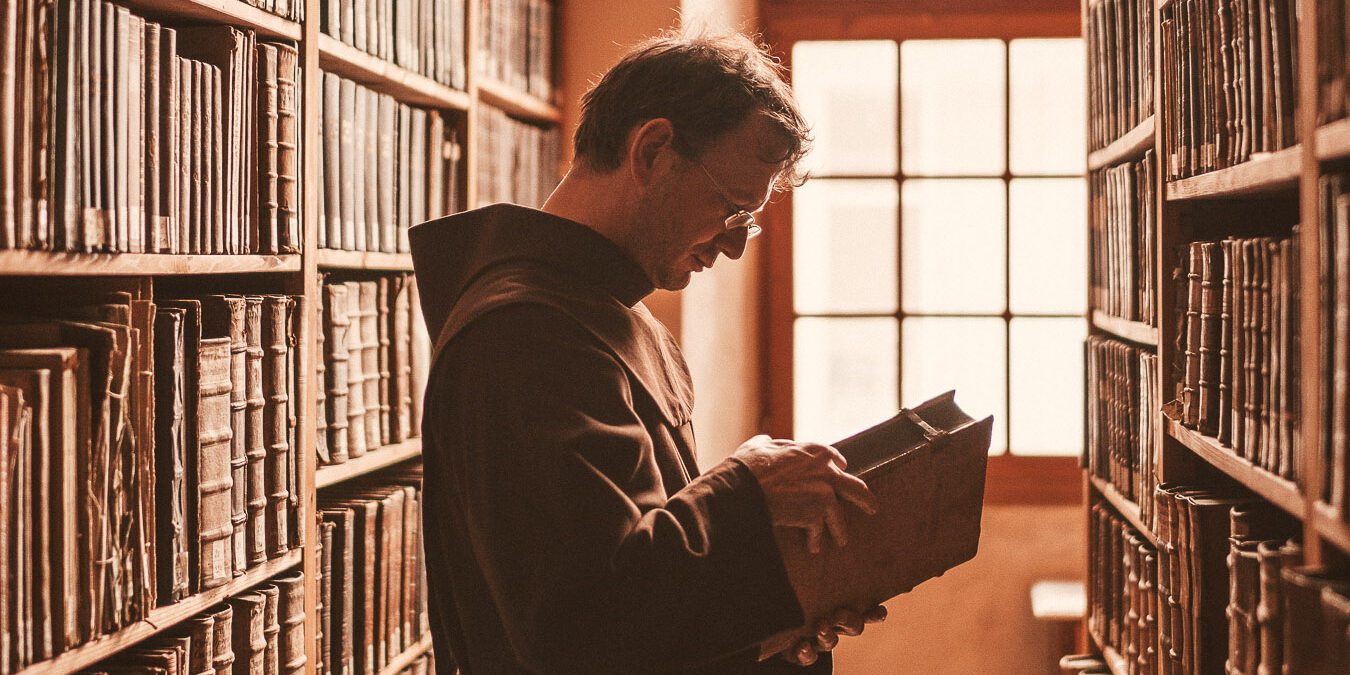 Franziskaner steht mit Buch in der Hand in Bücherei