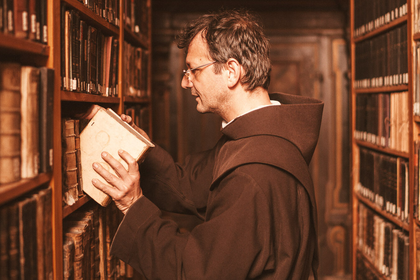 Franziskaner räumt Buch in Bibliothek auf